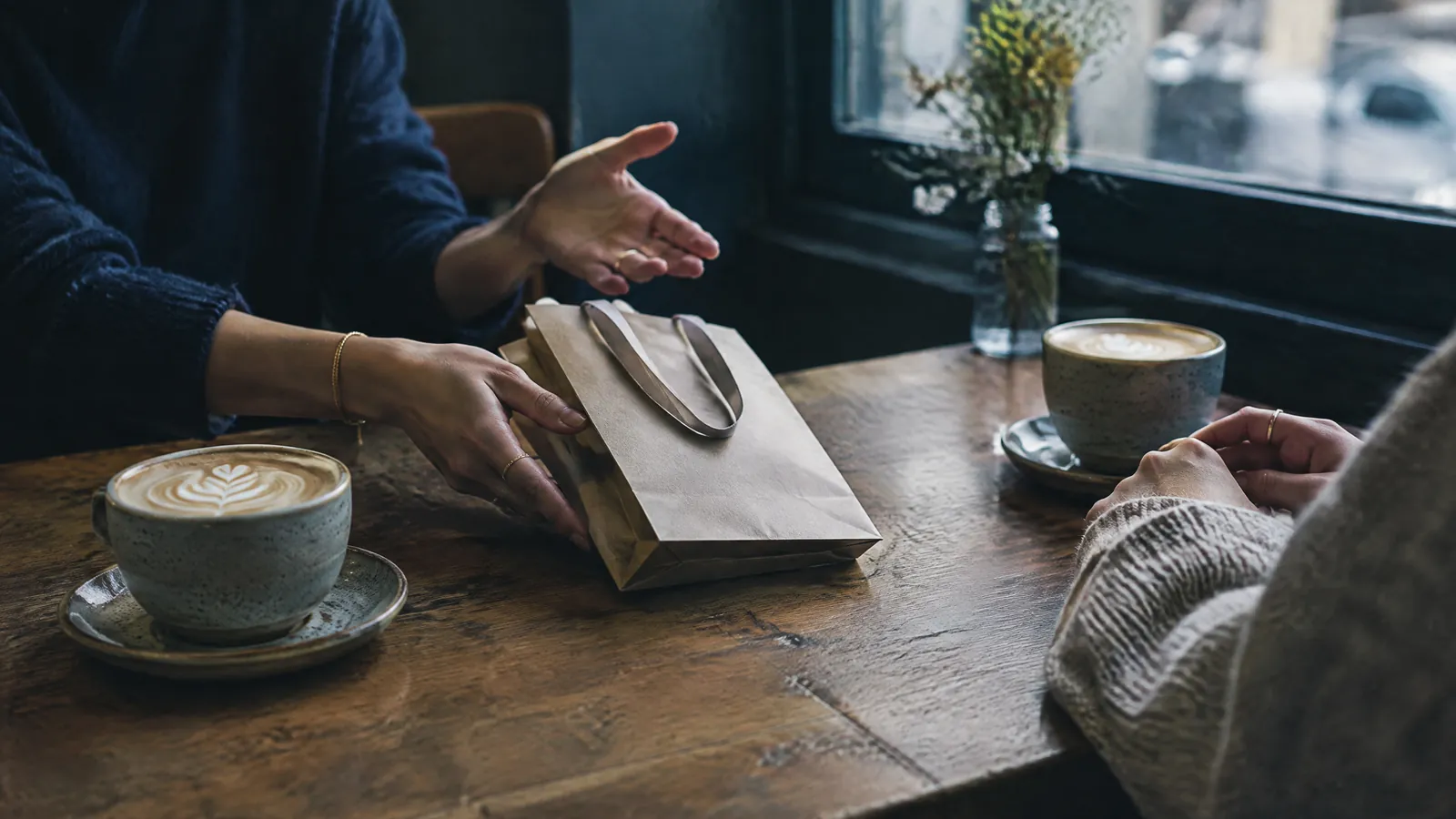 Two people at a cafe table with a paper bag and cups of coffee