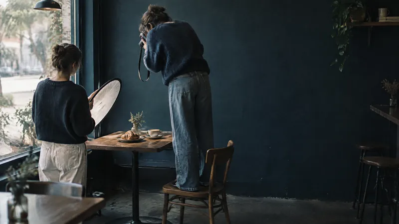 Two people photographing a styled plate on a cafe table by a window