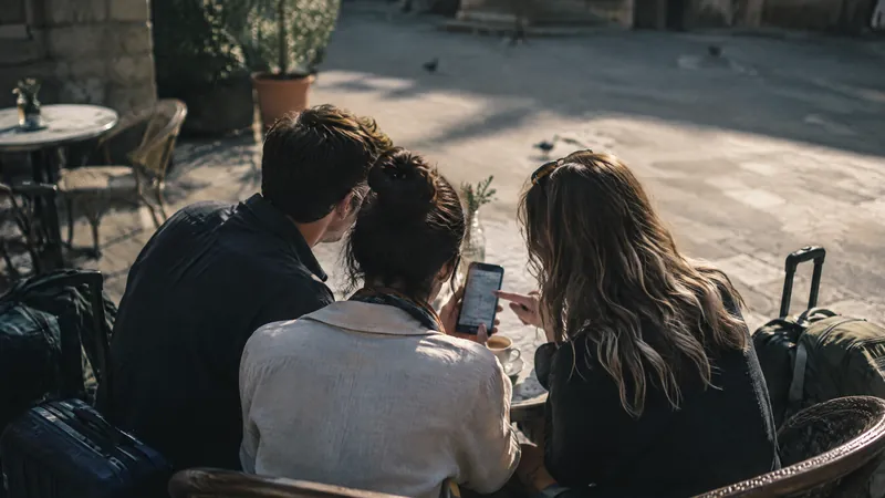 Three friends looking at a phone together at an outdoor cafe at sunset