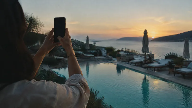 Hand raising a phone to photograph a clifftop pool at sunset
