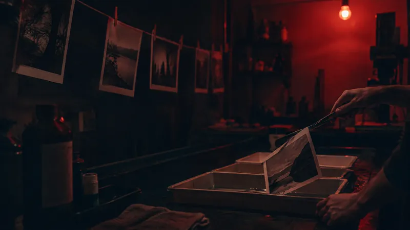 Hands opening a box in a darkroom hung with drying photographs