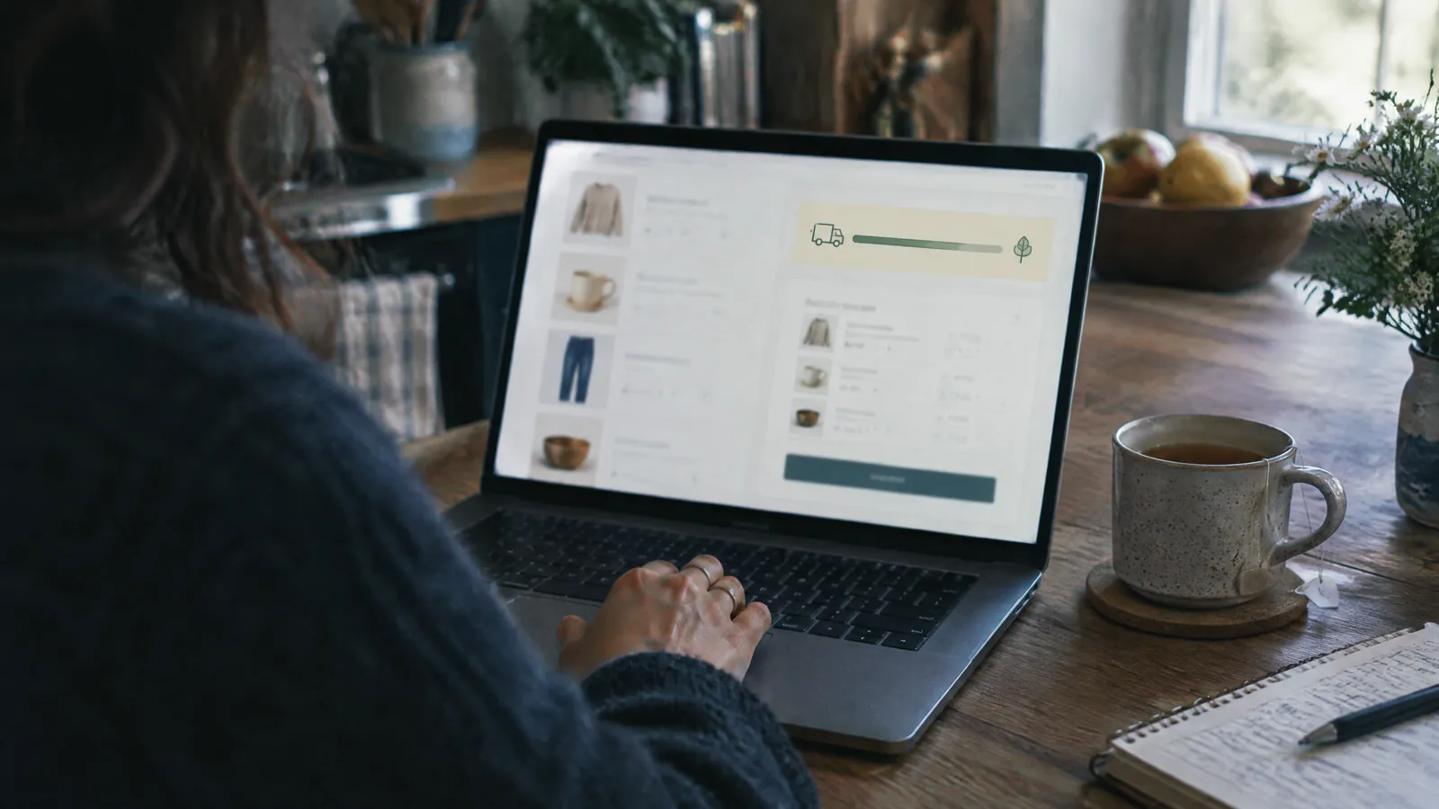 Person reviewing a shopping basket on a laptop at a kitchen counter