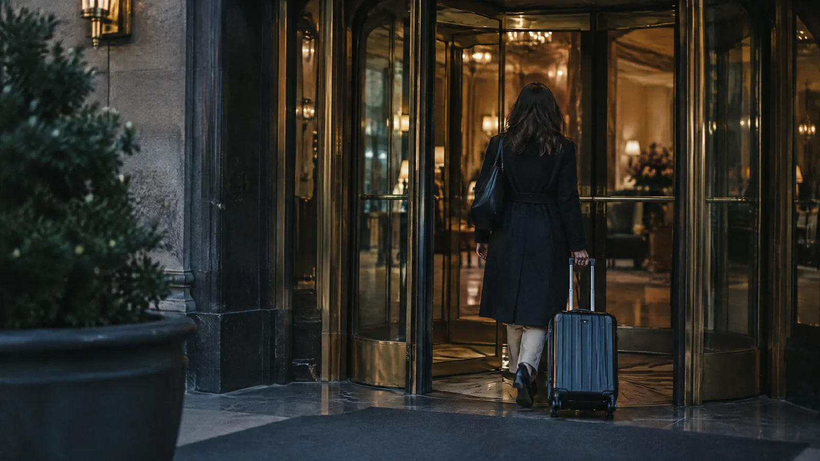 Person with a suitcase entering a hotel through a brass revolving door