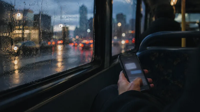 Hand holding a phone on a bus beside a rain-streaked window at night